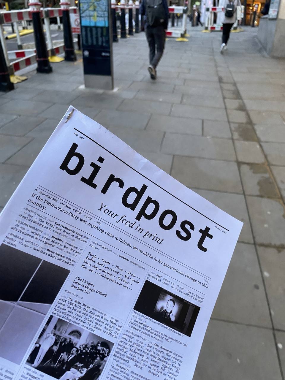 A printed Birdpost newspaper held up on a city street, showing a Bluesky feed laid out as a broadsheet.